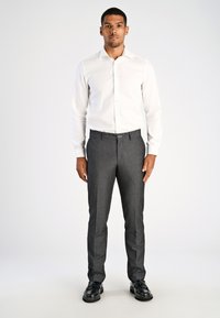 Camicia bianca a maniche lunghe con pattina di bottoni, abbinata a pantaloni grigi su misura con una texture sottile e scarpe eleganti nere.