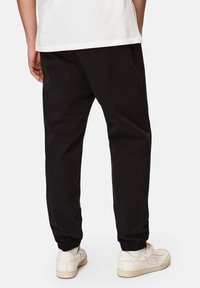 Schwarze Jogginghosen mit elastischen Bündchen, im entspannten Schnitt und aus weichem Material, kombiniert mit weißen Turnschuhen. Einfaches Design, ohne sichtbare Muster.