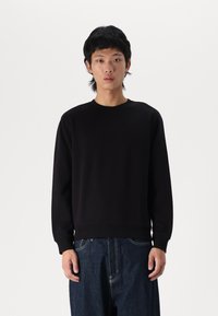 Sudadera negra de manga larga, con puños y dobladillo acanalados, diseño sencillo, fabricada en tejido suave, combinada con pantalones vaqueros oscuros de corte holgado.