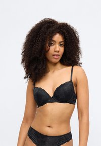 Čierna čipkovaná podprsenka s vypchávkami, kvetinovým vzorom a zvlnenými okrajmi. Ramienka sú nastaviteľné, poskytujú podporu a tvarovanú štruktúru.