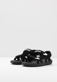 Infradito neri con cinturini regolabili in Velcro, materiale sintetico, design open-toe, soletta testurizzata e dettagli in logo bianco.
