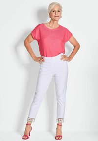 Roze top met korte mouwen en strass-accenten, gecombineerd met witte taps toelopende broeken met decoratieve rand bij de manchetten en roze hakken.
