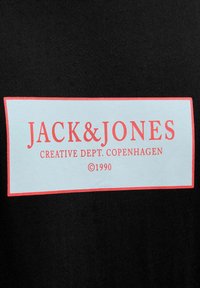 Camiseta de algodón negra con un logo rectangular azul claro y el texto rojo "JACK & JONES" y "CREATIVE DEPT. COPENHAGUE ©1990".