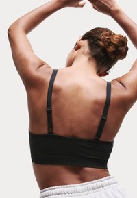 Svart sportbh med justerbara axelband, sömlös design och en bred band. Bakåtsikt visar en slät yta och minimal hårdvara.