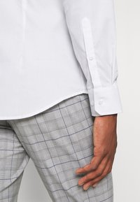 Witte lange mouwen shirt met knoopmanchetten, gecombineerd met grijze geruite broek met een subtiel ruitpatroon in marineblauw en wit.