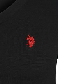Svart stickad tröja med V-ringning, med en liten röd broderad logotyp på vänster bröst.