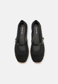 Black mesh slip-on shoes with a strap, featuring a textured sole and contrasting light-colored stitching around the edges. Brand name visible inside.