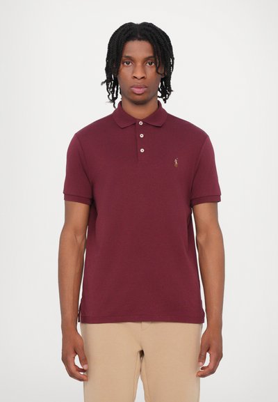 Polo burdeos con cuello, de manga corta y tres botones. Presenta un pequeño logo bordado en el pecho. Fabricado en algodón.