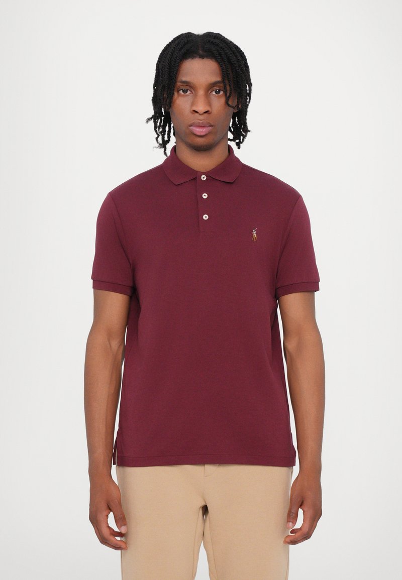 Burgundijas polo krekls ar apkakli, īsām piedurknēm un trim pogām. Ar mazu izšūtu logotipu uz krūtīm. Izgatavots no kokvilnas.