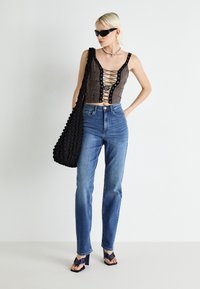 Rjav skrajšan top z vezalkami in črnimi detajli, modri trdi jeans z visokim pasom, črna torba z teksturiranim ročajem in vijoličasta sandala s peto.