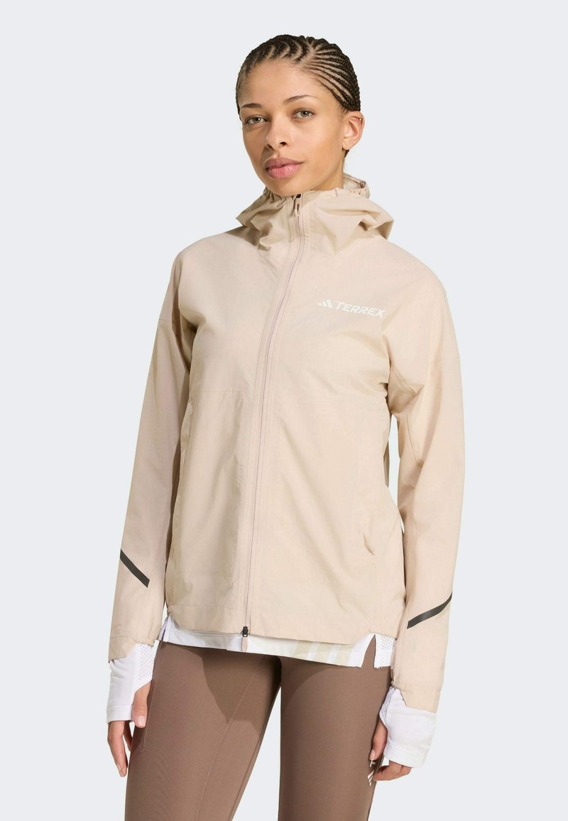 Veste légère beige à capuche avec fermeture éclair intégrale, poches latérales et accents réfléchissants sur les manches. Fabriquée en matériau lisse et résistant à l'eau.