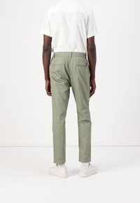 Zielone spodnie bawełniane o prostym kroju, z elastycznym paskiem w talii i dwoma tylnymi kieszeniami. Połączone z białym obuwiem i jasną koszulą.