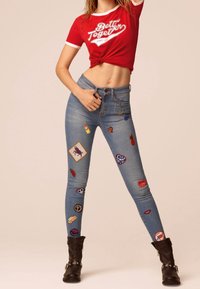 Smal denimjeans i ljusblått med färgglada lappar, inklusive hjärtan och frukter. Kombinerat med en röd T-shirt och svarta ankelstövlar.