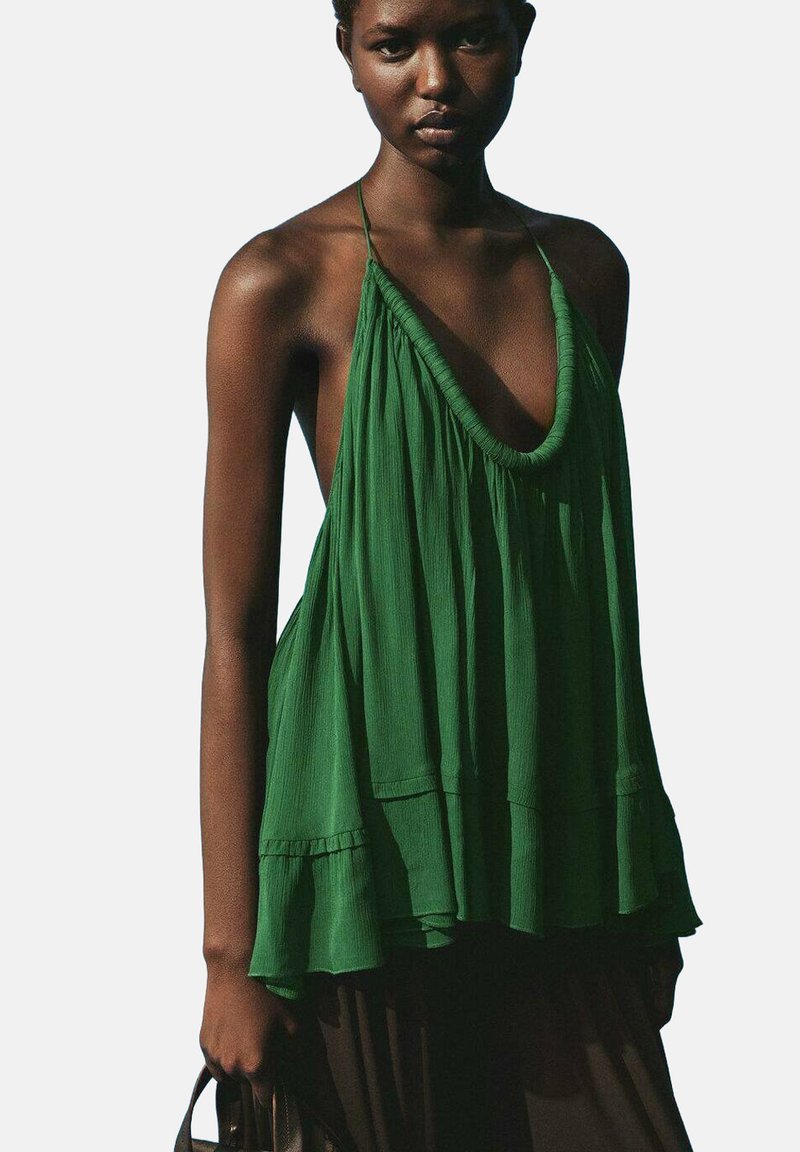 Zelený halter top vyrobený z lehkého materiálu, který má hluboký V-výstřih, volný střih a skládání textury, kombinovaný s černým spodním dílem.