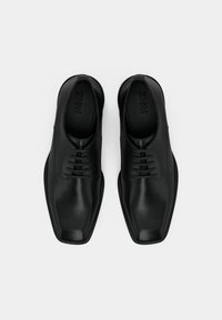 Chaussures habillées en cuir noir avec un bout carré, une texture lisse et six œillets pour les lacets. Design minimaliste avec une silhouette élégante.