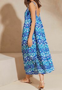 Vestido largo con una tela estampada en azul y azul verdoso, de corte holgado, con tirantes finos y un diseño de espalda baja. Acentuado con borlas.
