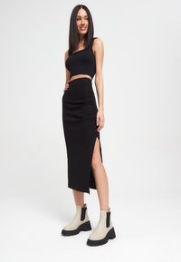 Top corto negro, falda negra ajustada con una abertura lateral y botines crema con suelas negras. Textura suave, diseño minimalista, silueta elegante.