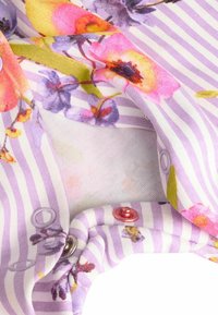 Dryžuota medžiaga su violetiniais ir baltais raižiniais, kuriame yra gėlių raštų rožinės, geltonos ir lavandinės spalvos. Pridedami violetiniai ir raudoni spaudimo mygtukai.