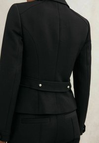 Schwarze taillierte Jacke mit passgenauem Design, strukturierten Schultern, doppelter Rückenbelüftung und einem Taillengürtel mit silbernen Knöpfen.