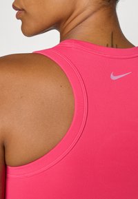 Top sportiv roz cu guler rotunjit, având o textură netedă și un mic logo alb Nike pe spate.