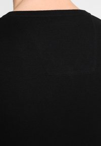 Svart stickad tröja med ribbad halsringning och bakdetalj, med en mjuk textur och enhetlig färg. Inga mönster eller extra detaljer.