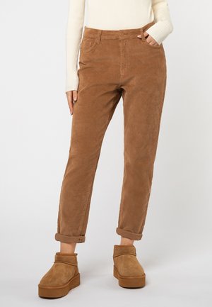 Brown corduroy trousers with a straight cut, rolled cuffs, and five-pocket design, paired with tan suede ankle boots.