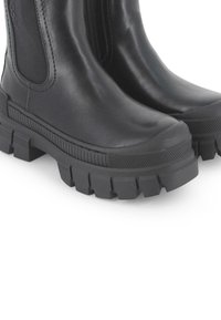 Botas de tobillo de cuero negro que cuentan con una suela de goma texturizada, paneles elásticos laterales y un diseño de punta redondeada. Suela con un fuerte relieve para mayor tracción.