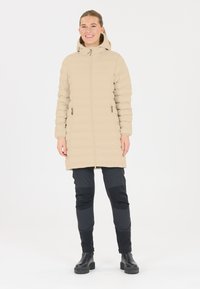 Beige puffer coat med hætte, horisontal syning design, front lynlås lukning og to sidelommer. Bæres med sorte bukser og chunky støvler.