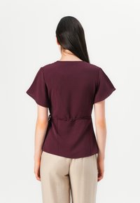 Maroon top with short flutter sleeves, fitted waist, and a slightly flared hem. Smooth texture, lightweight fabric, stylishly cinched at the waist.