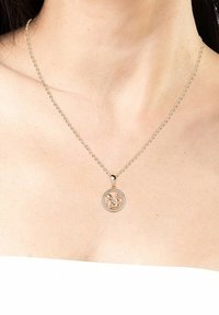 Collana in tono oro con un pendente rotondo che presenta un design centrale circondato da piccole pietre trasparenti. La catena ha un classico motivo a maglie.