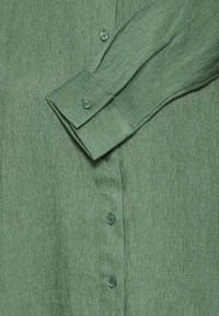 Chemise à manches longues verte avec un col replié et des boutons visibles sur le devant, fabriquée à partir d'un tissu texturé.