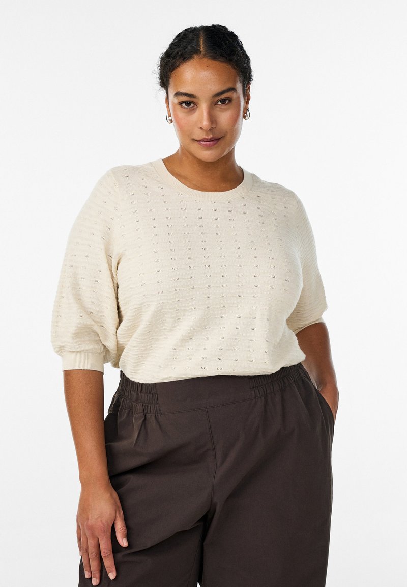 Top de punto texturizado color crema con cuello redondo y mangas cortas y voluminosas. Combinado con pantalones de cintura elástica en marrón oscuro.