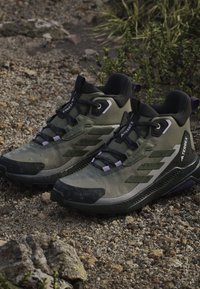 High-top hiking shoes in dark green, featuring a textured synthetic upper, black accents, and reflective elements. Lightweight and durable sole.