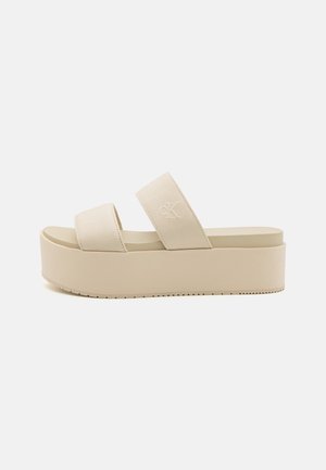 Sandalias de plataforma beige con dos correas anchas, confeccionadas en tela, que presentan una suela texturizada y un sutil detalle de logo. Diseño suave y minimalista.