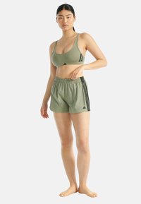 Olivově zelená sportovní podprsenka s tenkými ramínky, spárovaná s odpovídajícími šortkami s černými bočními pruhy a elastickým pasem.