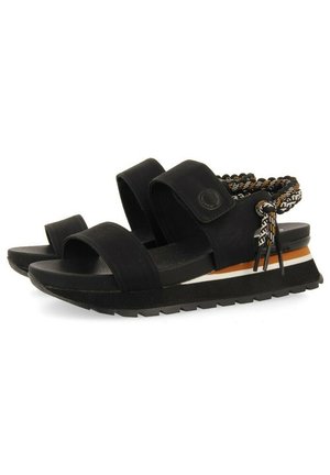 Las sandalias negras cuentan con amplias correas de tela y una suela gruesa con un acabado texturizado. Los acentos trenzados son de tonos negro y marrón.