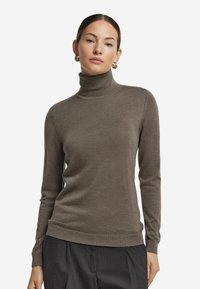 Brun polotröja gjord av mjukt stickad tyg, med långa ärmar, en ribbad krage och en figurnära silhuett.