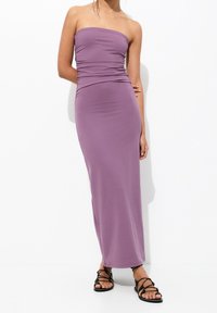 Robe maxi sans manche violet avec un corsage ajusté et un détail froncé à la taille, associée à des sandales plates noires à lanières. Tissu lisse.