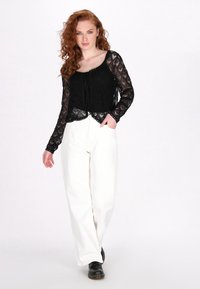 Top din dantelă neagră, cu mâneci lungi, modele decorative și o fundă în față, asortat cu pantaloni albi, lejeri și pantofi negri.