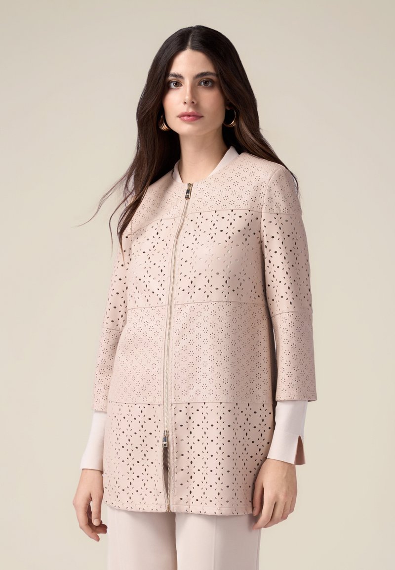 Veste perforée rose clair avec fermeture éclair, col rond, manches trois-quarts et coupe structurée, mettant en valeur un motif de surface texturé.