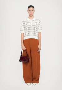 Weißes gestricktes Poloshirt mit horizontalen Streifen, kombiniert mit weit geschnittenen braunen Hosen und einer kleinen burgunderfarbenen Handtasche aus Lackleder. Cremefarbene Schuhe runden das Outfit ab.