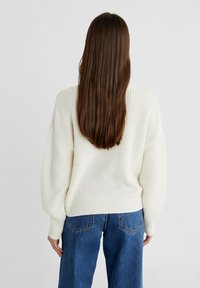 Ivoorkleurige gebreide trui met een losse pasvorm, verlaagde schouders en geribde manchetten, gecombineerd met een high-waisted blauwe spijkerbroek. Gestructureerde stof.