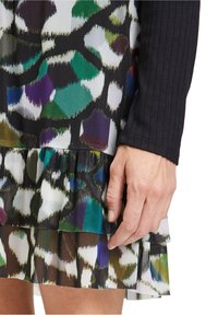 Dress featuring a colorful abstract animal print with green, purple, and black tones. The hem has a tiered ruffle detail. Long black ribbed sleeve.