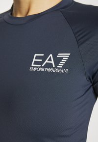 Marineblauw sportshirt van textiele stof, met een wit EA7 Emporio Armani-logo op de borst en een getailleerd ontwerp.