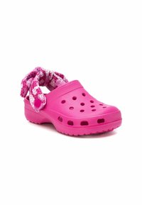 Zueco rosa sin cordones con agujeros de ventilación en los laterales y un lazo decorativo de tela estampada en el talón, fabricado con un material ligero y acabado texturizado.
