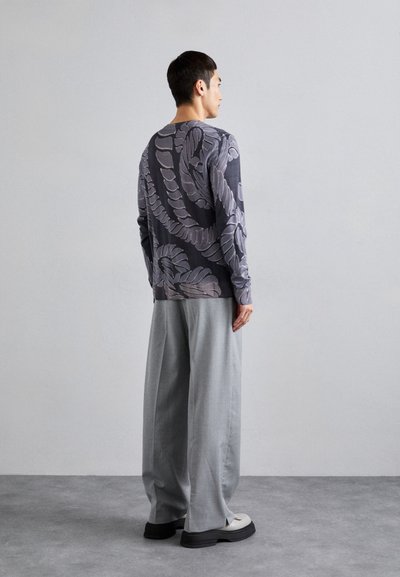 Cămașă cu mânecă lungă de culoare gri închis, cu un design floral mare în gri mai deschis, asortată cu pantaloni lejeri gri deschis și pantofi masivi negri.