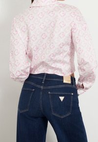 Vit skjorta med rosa geometriskt mönster, ihopparad med mörkblå denimjeans som har en triangel-logo och detaljeringar på bakfickorna.