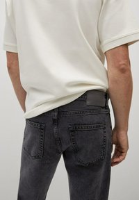 Tummanharmaat farkut, joissa on suora leikkaus, takataskut ja teksturoitu pinta. Yhdistetty yksinkertaiseen valkoiseen poolopaitaan.