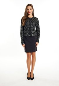 Cardigan negru cu design structurat și model cu paiete, asortat cu o fustă tip creion neagră și pantofi cu vârf ascuțit negri.
