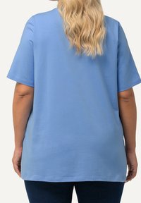 Ljusblå kortärmad skjorta med en avslappnad passform. Slät textur, rund halsringning och rak nederkant. Sedd bakifrån med lösa, vågiga lockar.